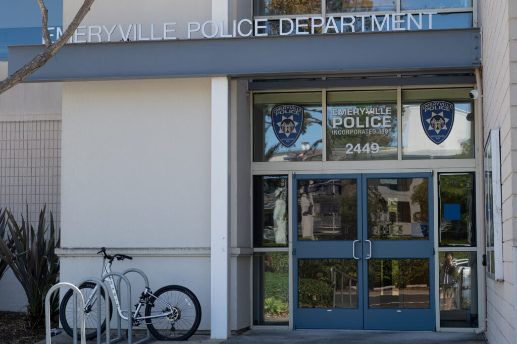 A shot of the front door of Emeryville Police Department. On the left botton is a bicycle locked on a bike parking pole.