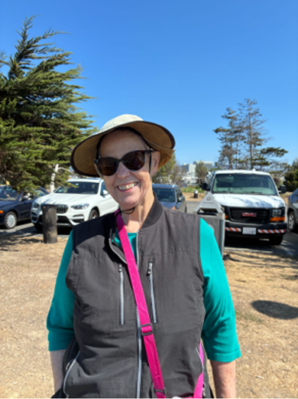 A middle-aged woman with a sun hat and sunglasses stand in front of four vehicles