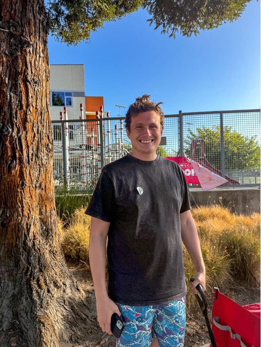 A portrait of a man standing beside a tree in front of metal fences