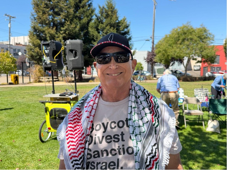 A portrait of a person who wears a baseball cap, sunglasses, and a keffiyeh