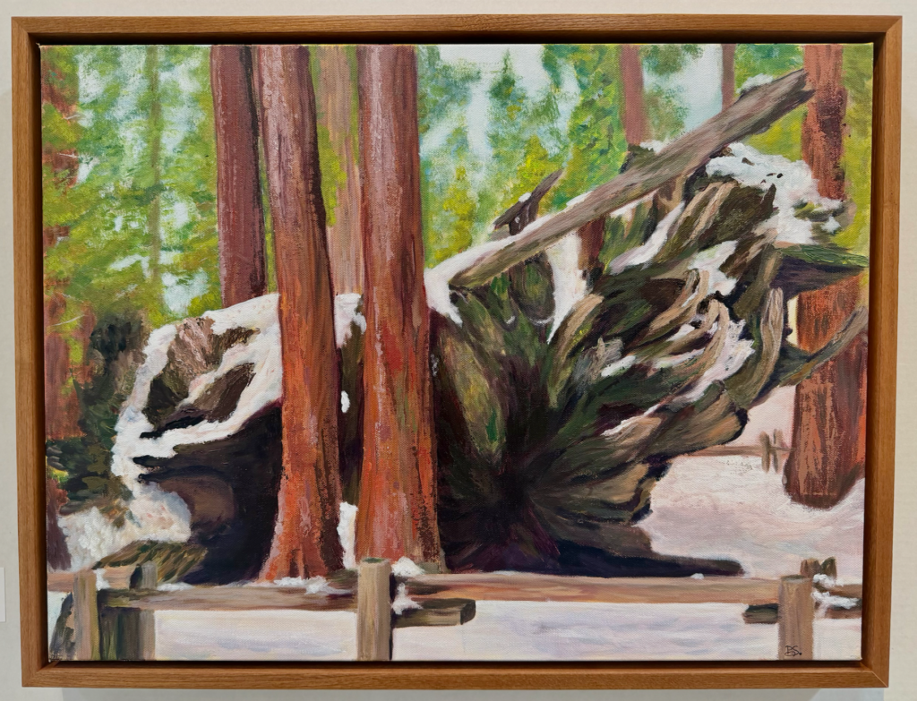 A framed painting shows a fallen large tree trunk covered with snow amid tall standing trees.